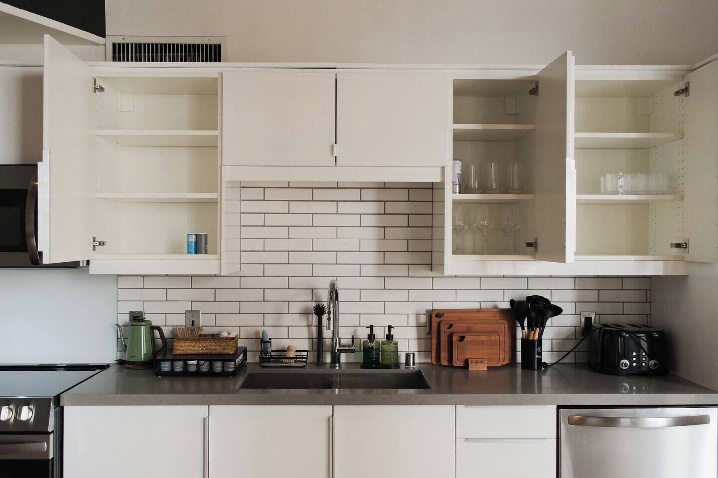 A modern kitchen with white cabinetry, a tiled backsplash, and various kitchen appliances and utensils.