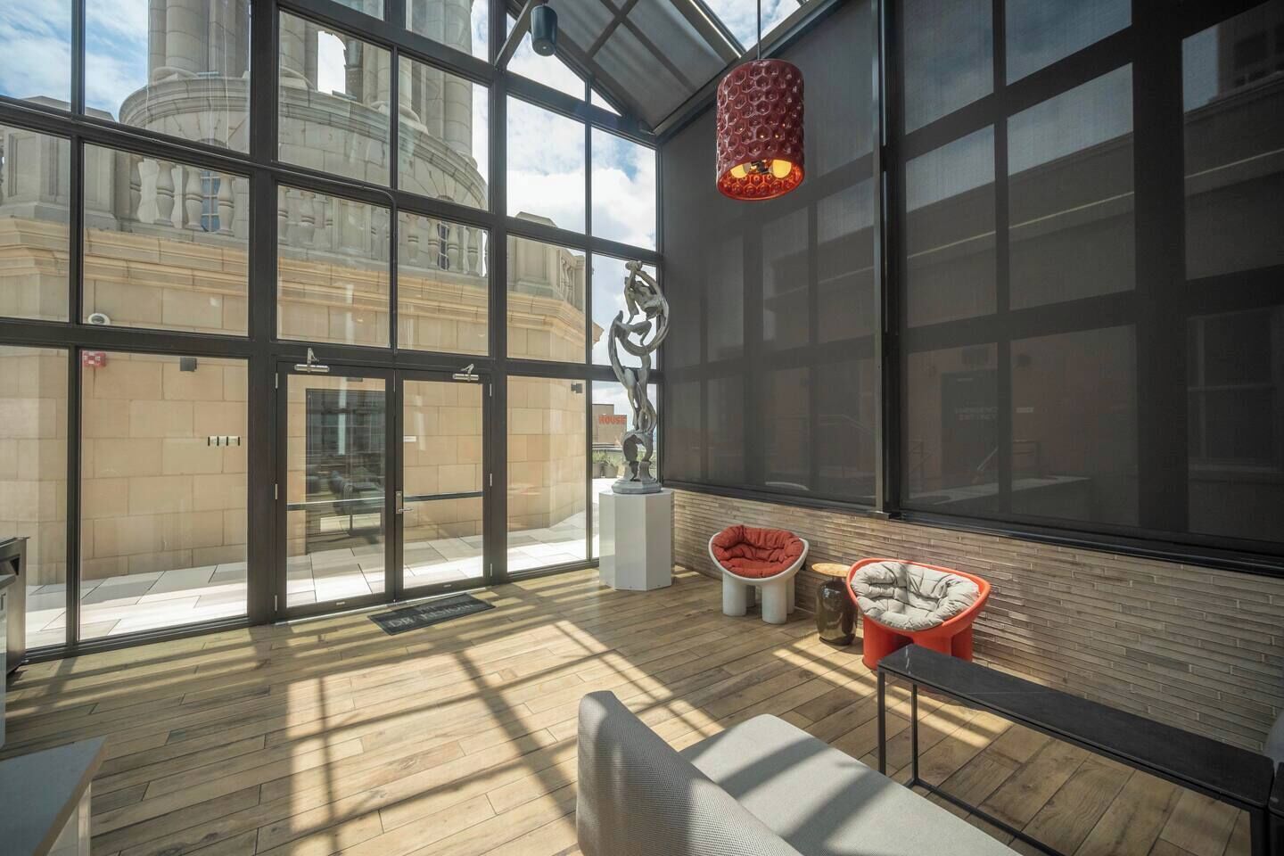 A spacious room with large windows, a wooden floor, and modern furniture including a red chair and a sofa.
