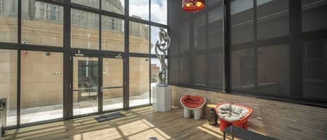 Amplia habitación con ventanas grandes, piso de madera y mobiliario moderno, incluyendo una silla roja y un sofá.