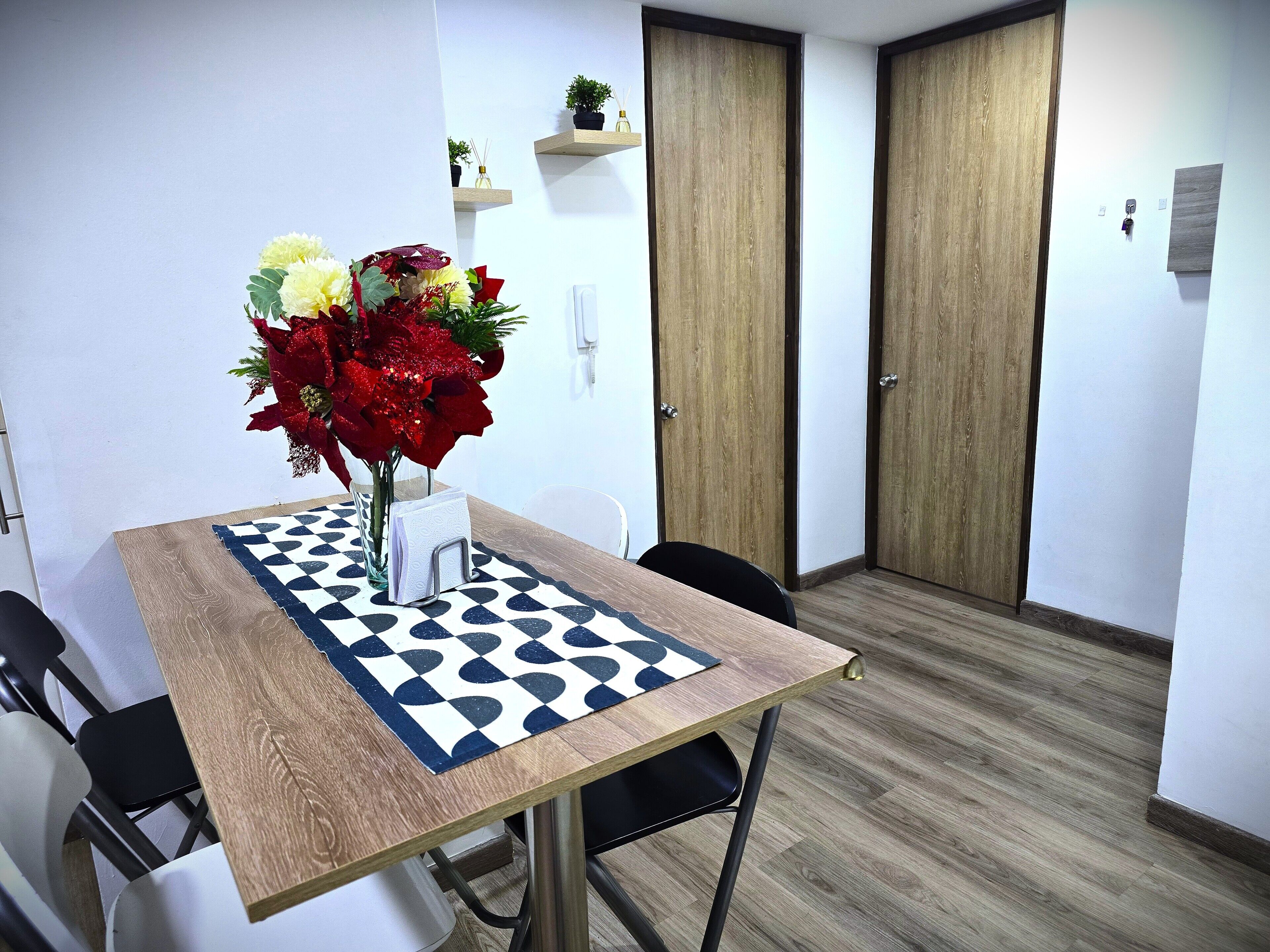 Ein Zimmer mit einem Holztisch, Stühlen, einer karierten Tischdecke und einer Vase mit Blumen.
