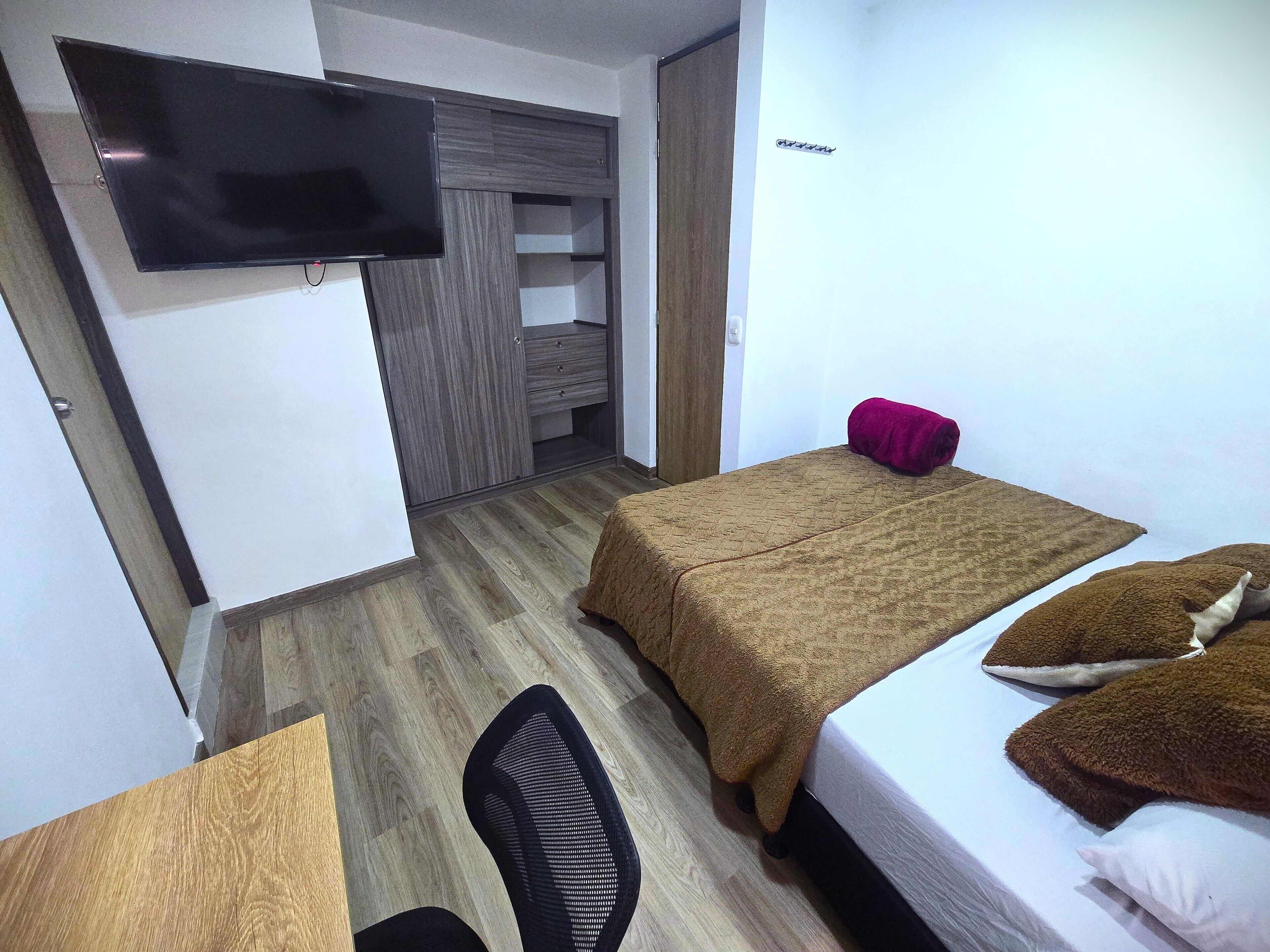 A hotel room with two beds, a desk, a chair, a TV, and a wardrobe.