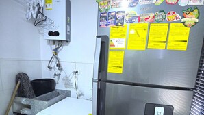 Kompakti keittiö, jossa on ruostumattomasta teräksestä valmistettu jääkaappi, pesukone ja vesihana.