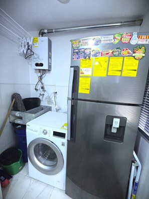 Eine kompakte Küche mit einem Edelstahl-Kühlschrank, einer Waschmaschine und einem Wasserspender.