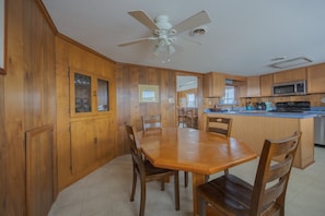 A kitchen with wooden cabinets, a dining table, chairs, a ceiling fan, and a microwave. - 4755 - The OBX Rx, Semi-oceanfront! (Kitty Hawk)