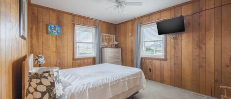A bedroom with wooden walls, a bed, a TV, and a window with blinds.