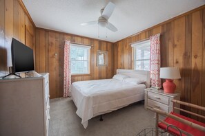 A bedroom with a bed, a television, a desk with a lamp, and wooden walls. - 4755 - The OBX Rx, Semi-oceanfront! (Kitty Hawk)