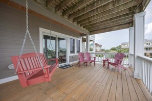 A covered porch with wooden flooring, two Adirondack chairs, and a swing chair. - 1822 - Our Happy Place By The Sea, Corolla Retreat | Saltwater Pool & Arcade Game (Corolla)