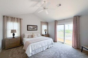 Ein Schlafzimmer mit einem großen Bett, zwei Nachttischen inklusive Lampen, einem Deckenventilator und Blick durch eine Schiebeglastür.