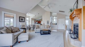 A spacious living room with a fireplace, a dining area, and a kitchen in the background. - 1822 - Our Happy Place By The Sea, Corolla Retreat | Saltwater Pool & Arcade Game (Corolla)