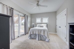 A bedroom with a bed, a ceiling fan, a window with blinds, a door, and a view of a deck. - 1822 - Our Happy Place By The Sea, Corolla Retreat | Saltwater Pool & Arcade Game (Corolla)