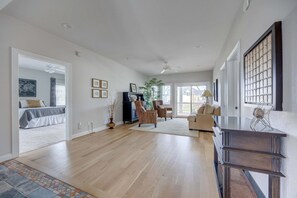 A spacious living room with hardwood flooring, a large window, and a view of the outside. - 1822 - Our Happy Place By The Sea, Corolla Retreat | Saltwater Pool & Arcade Game (Corolla)