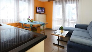 A modern living room with a sofa, a dining table with chairs, a kitchen area with a countertop, and a television mounted on the wall. - GOLF Apartments Appartement/Fewo 4-Bettwohnung Nr. 3 by Interhome (Saas-Fee)
