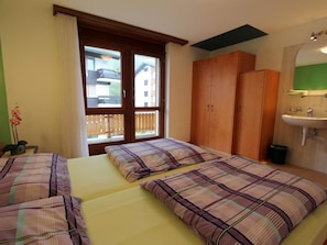 Ett hotellrum med två sängar, ett fönster med utsikt över byggnader, en garderob i trä och ett badrum med handfat.