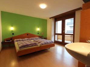 A bedroom with a bed, two bedside lamps, a window with a view, and a bathroom with a sink. - GOLF Apartments Appartement/Fewo 4-Bettwohnung Nr. 3 by Interhome (Saas-Fee)