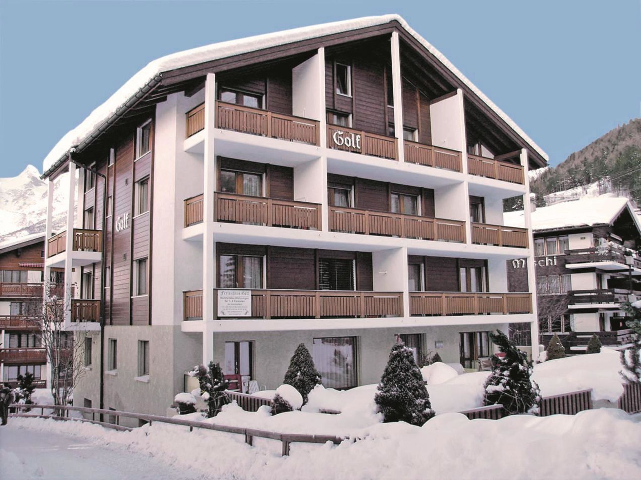 Ein mehrstöckiges Hotel mit Balkonen, einem Schild, das es als Golfresort kennzeichnet, und verschneiter Umgebung.