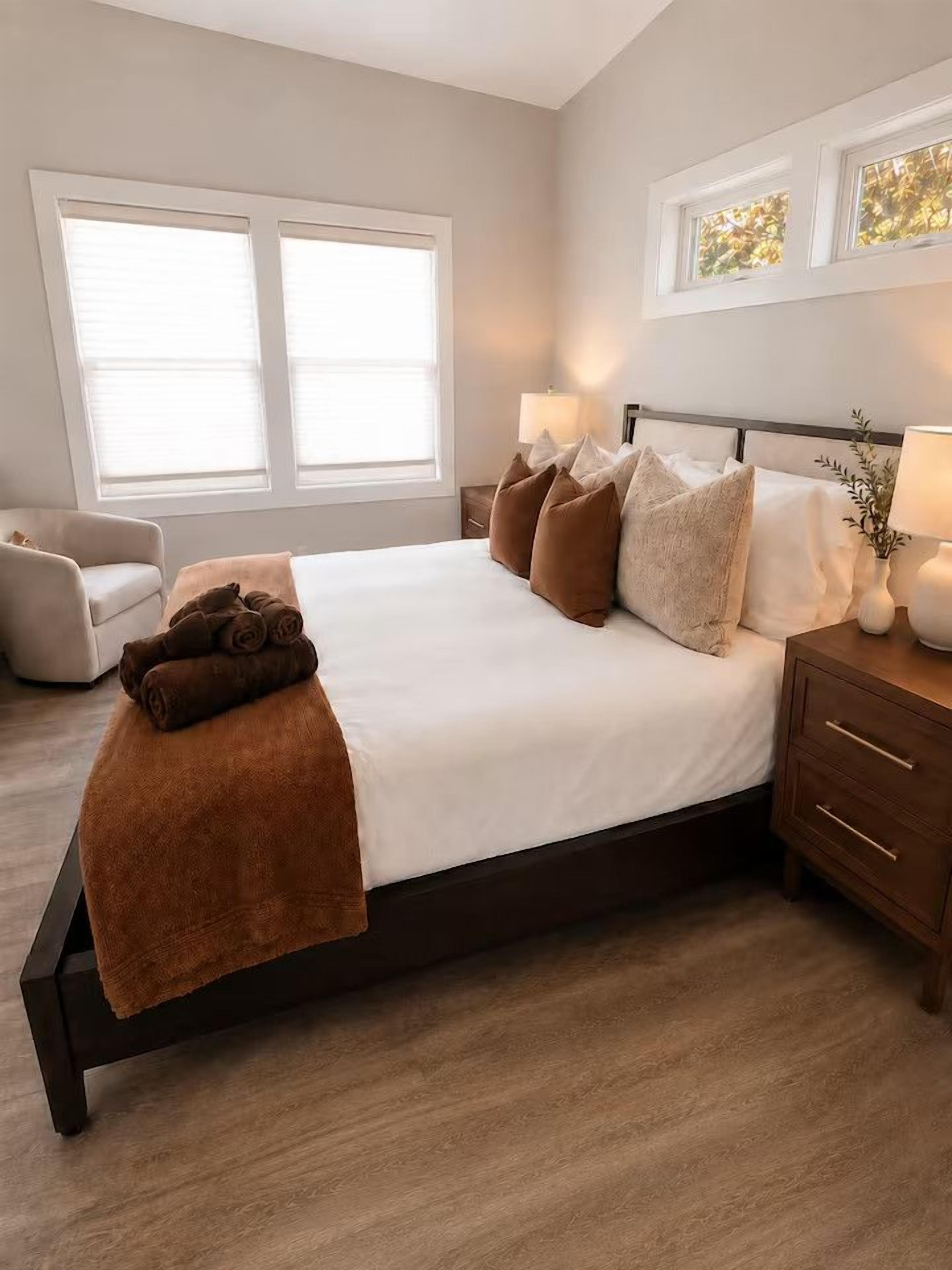 A bedroom with a bed, bedside tables, a chair, and windows.