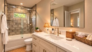 Une salle de bain moderne avec une douche à l’italienne en pierre, une baignoire, des toilettes et un meuble-lavabo avec un évier et un miroir.