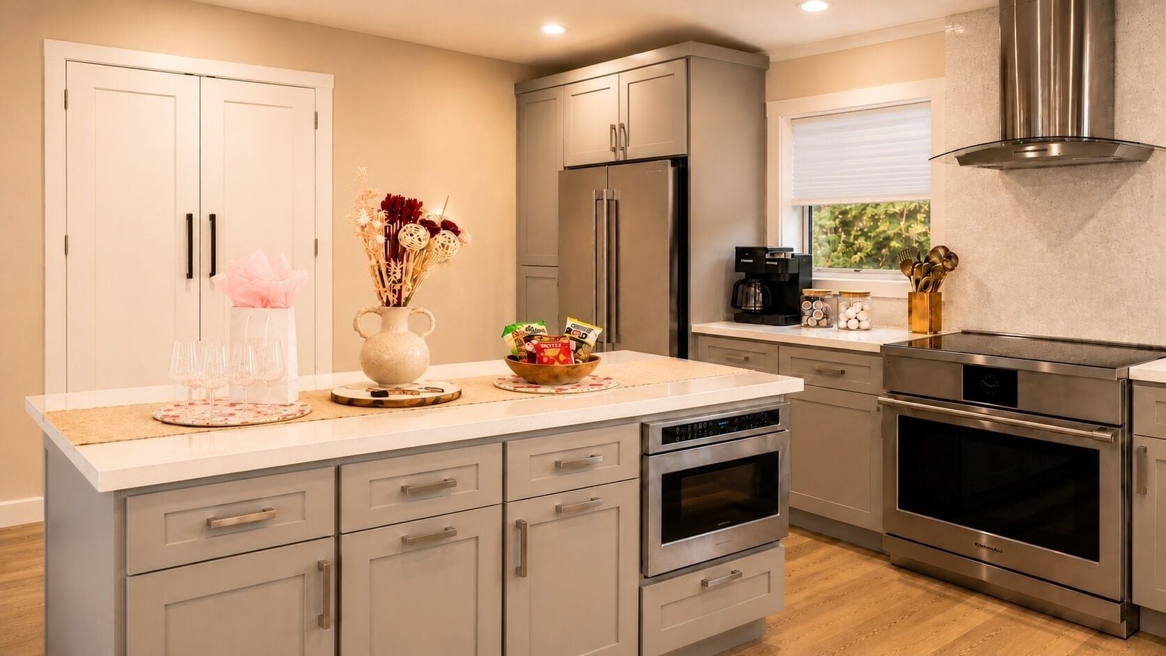 A modern kitchen with stainless steel appliances, a central island with a vase and snacks, and a window with a view.