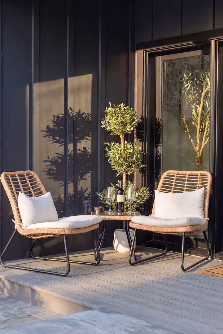 Un espace extérieur moderne, aménagé avec deux fauteuils en osier et une petite table, entouré de plantes en pot et d'une vitrine.