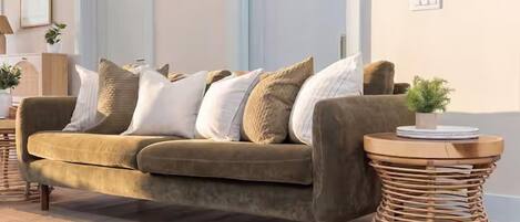A living room with a sofa, cushions, a round side table, and a small plant.