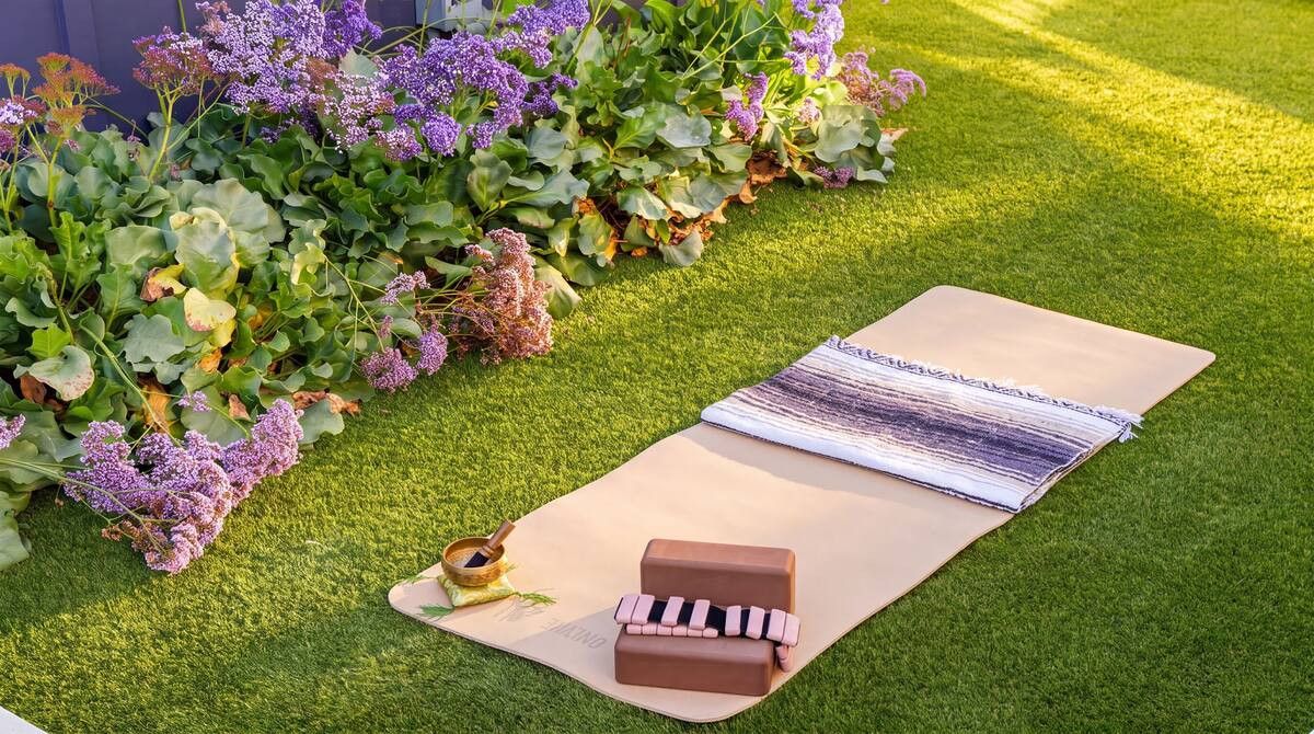Eine Yogamatte auf Rasenteppich, zusammen mit einem Holzklotz und einer aufgerollten Matte.
