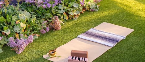 A yoga mat on artificial grass with a wooden block and a rolled-up mat.