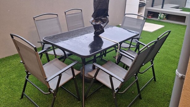Eine Außenpatio mit rundem Tisch und Stühlen, umgeben von Kunstrasen.