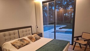 Ein Schlafzimmer mit einem großen Bett, einem Nachttisch, einem Sessel und Blick auf einen Außenpool.