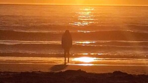 Eine Silhouette einer Person, die am Strand steht, während die Sonne im Hintergrund untergeht.