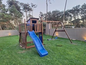 A wooden play structure with a slide and swings in a grassy backyard. - House 1 (Esposende)