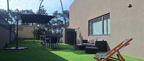 Une terrasse extérieure moderne, dotée d’un gazon synthétique, d’un espace salon et d’une grande fenêtre.