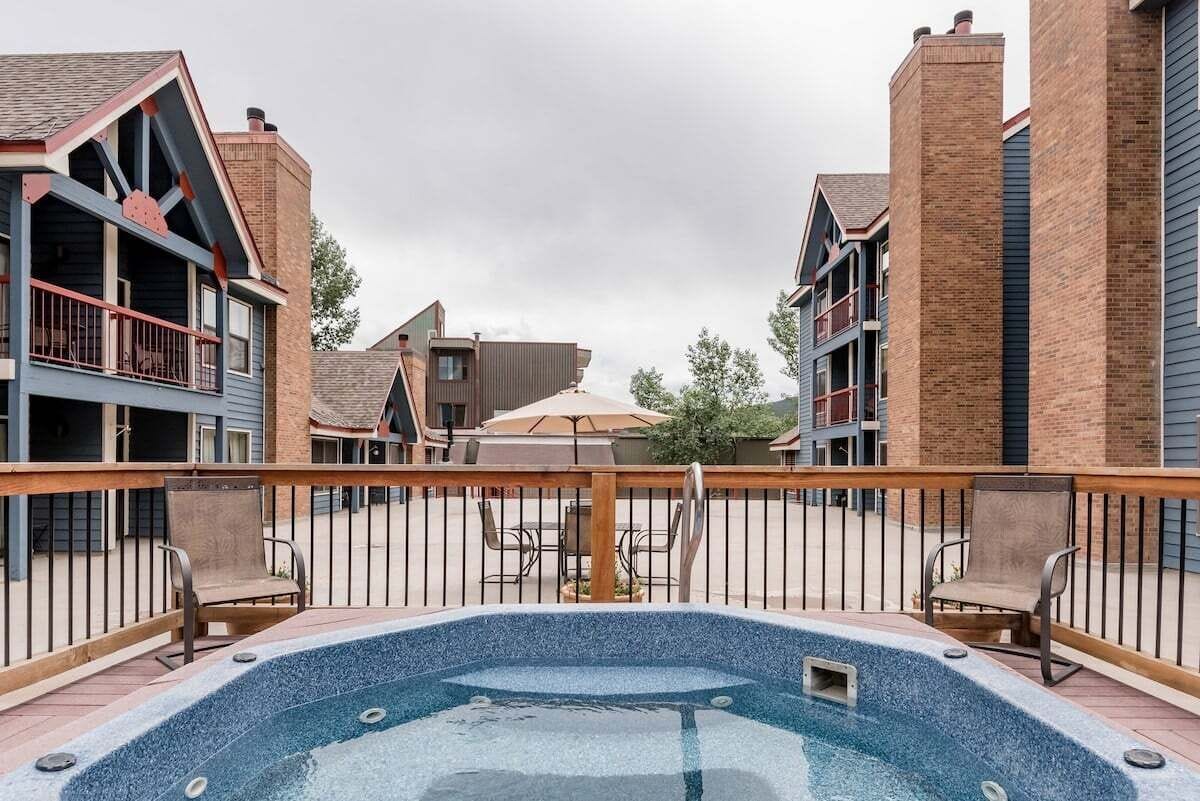 A rooftop pool area with a wooden deck, surrounded by brick buildings with balconies.