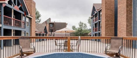 A rooftop pool area with a wooden deck, surrounded by brick buildings with balconies.