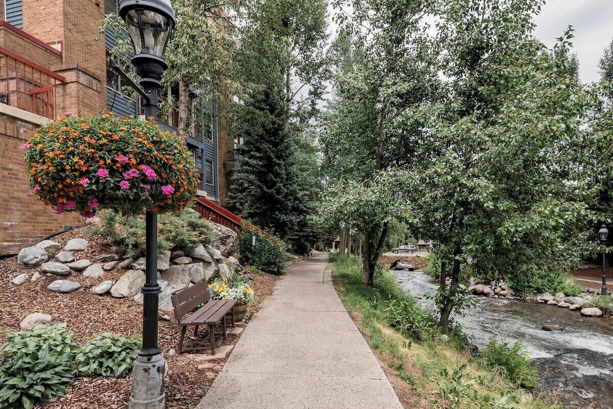 A pathway alongside a river with a bench and a hanging flower basket.
