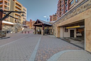A paved walkway leading to a building with a stone facade, a covered entrance, and a sign indicating a pay & display parking area. - Peak 9 Inn 4512: Stellar Views - Downtown & Ski In Ski Out @ Base of Peak 9 (Breckenridge)