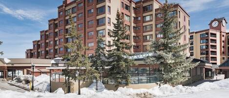 A multi-story hotel with a snow-covered ground, a clock tower, and a central courtyard with trees.