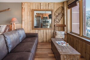 A cozy living area with a brown leather sofa, a wooden coffee table, and a mirror reflecting a kitchen area. - Peak 9 Inn 4512: Stellar Views - Downtown & Ski In Ski Out @ Base of Peak 9 (Breckenridge)