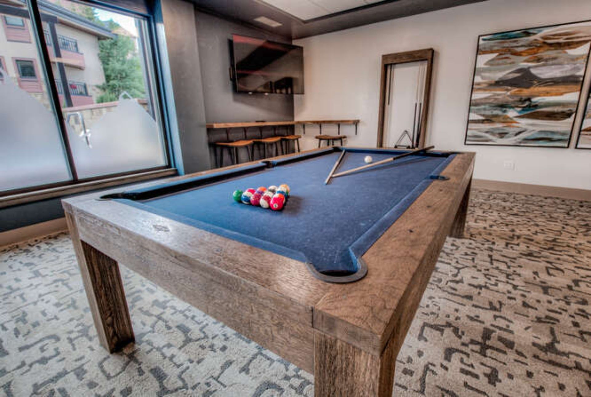 A pool table with balls, a mirror, and a painting on the wall.