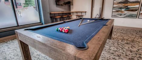 A pool table with balls, a mirror, and a painting on the wall.