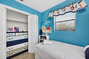 Ein Schlafzimmer mit einem Bett, einem Schrank mit Schubladen, einem Fenster mit Jalousien und einer Wand mit einem Vorhang im Seestil.