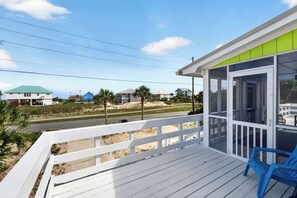 A wooden deck with a white railing, a blue chair, and a view of houses and beach in the background. - Key Lime Cottage - 250 Steps to Beach, Beach Gear Credit Included, Recent Renovations (St. George Island)