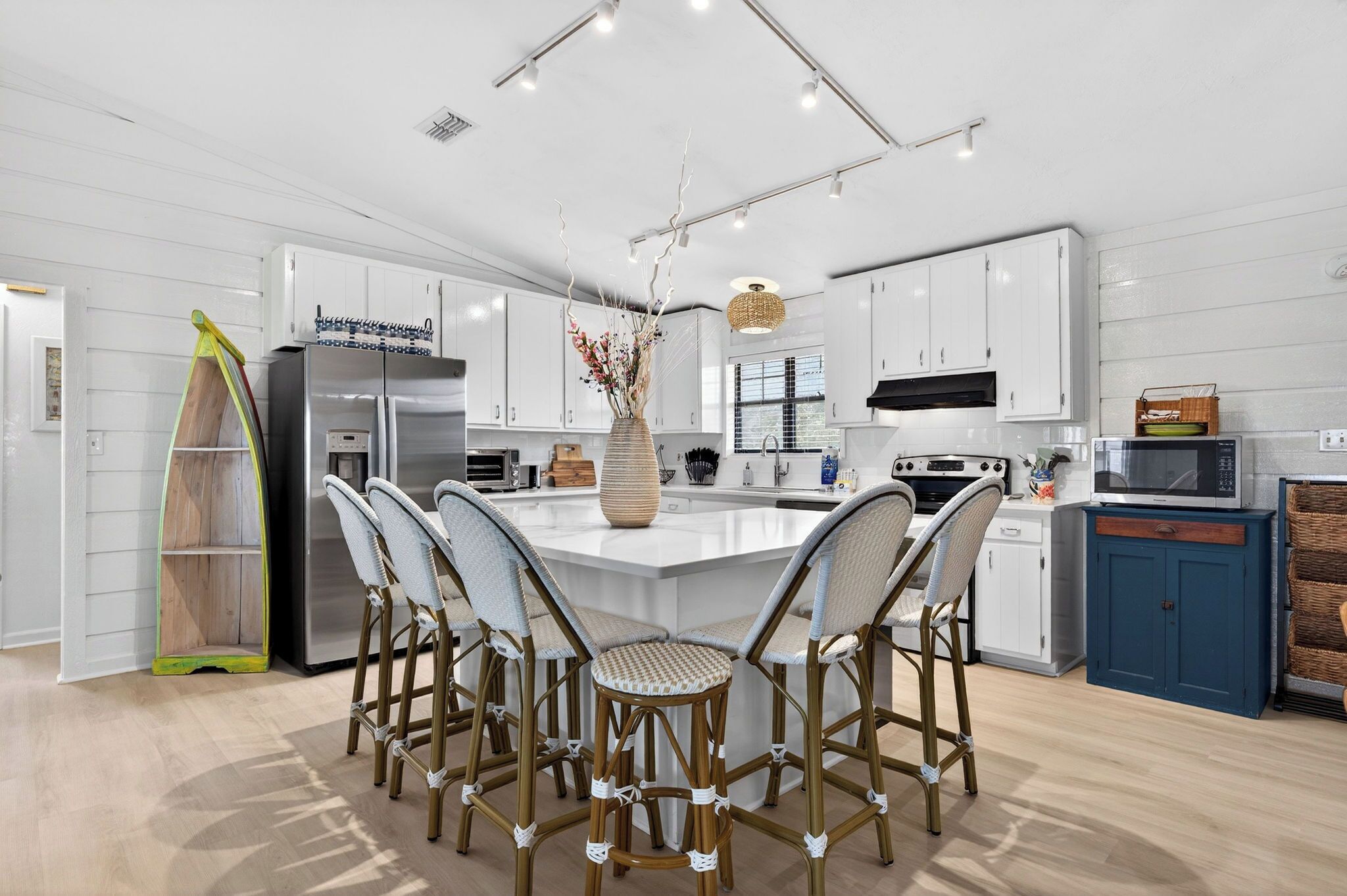 Una cocina moderna con armarios blancos, una isla central con sillas, un refrigerador y un microondas.