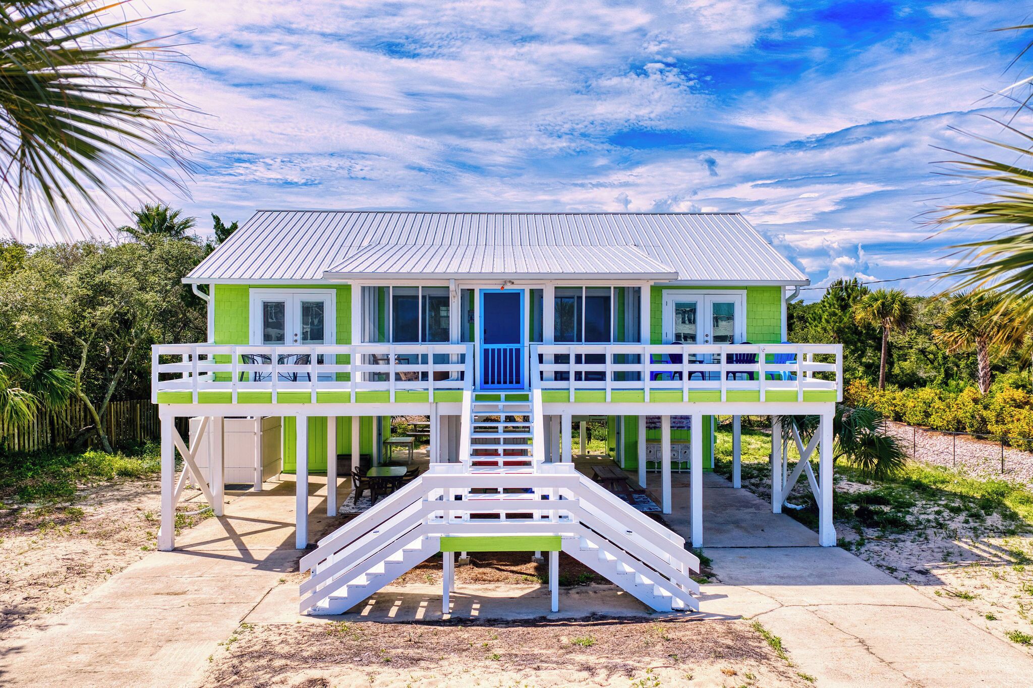 Ein zweistöckiges Haus mit blauer Tür, weißen Geländern und einer Veranda mit Stühlen.