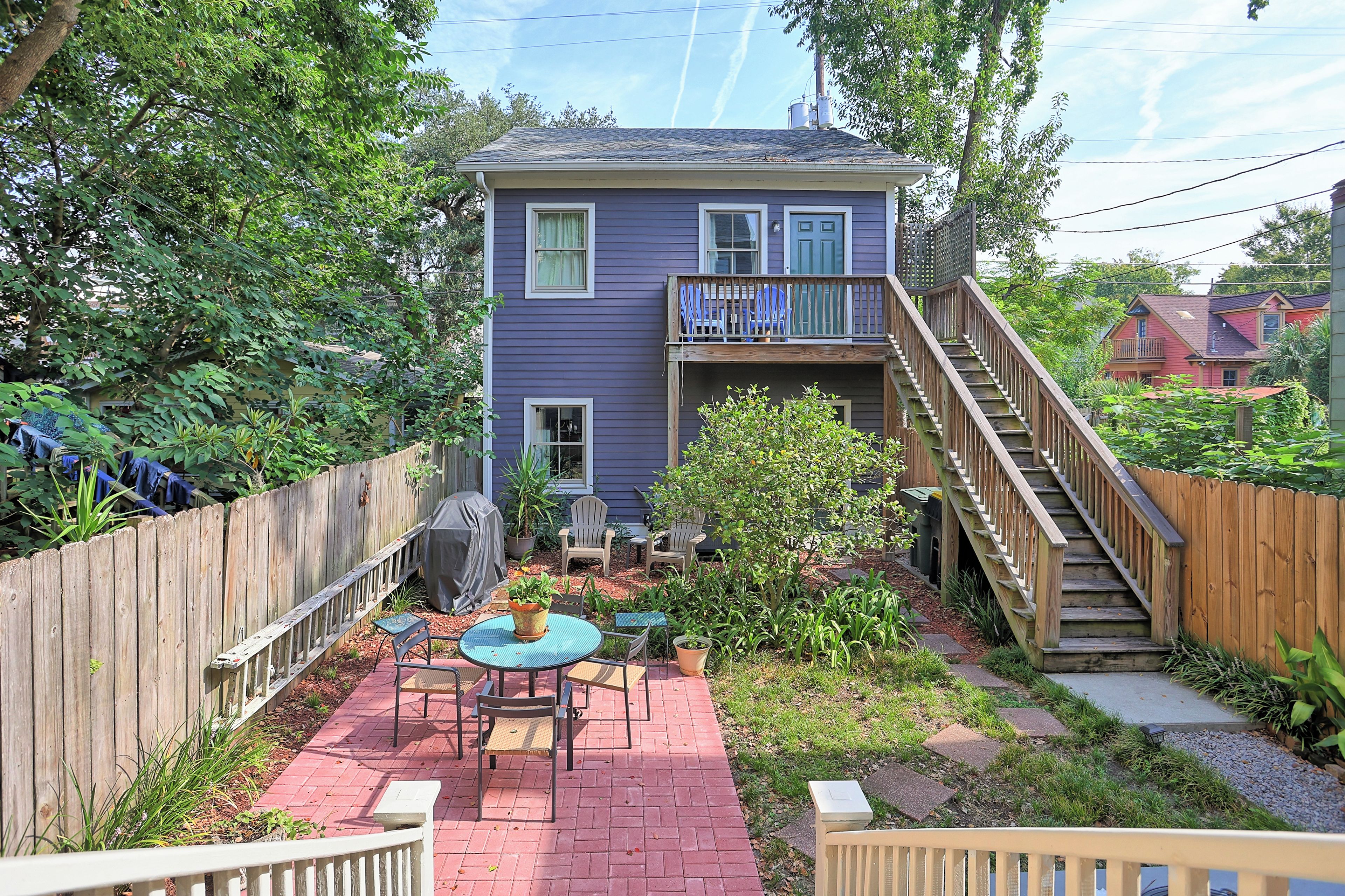 A two-story house with a covered patio area, a wooden staircase, and a fenced backyard.