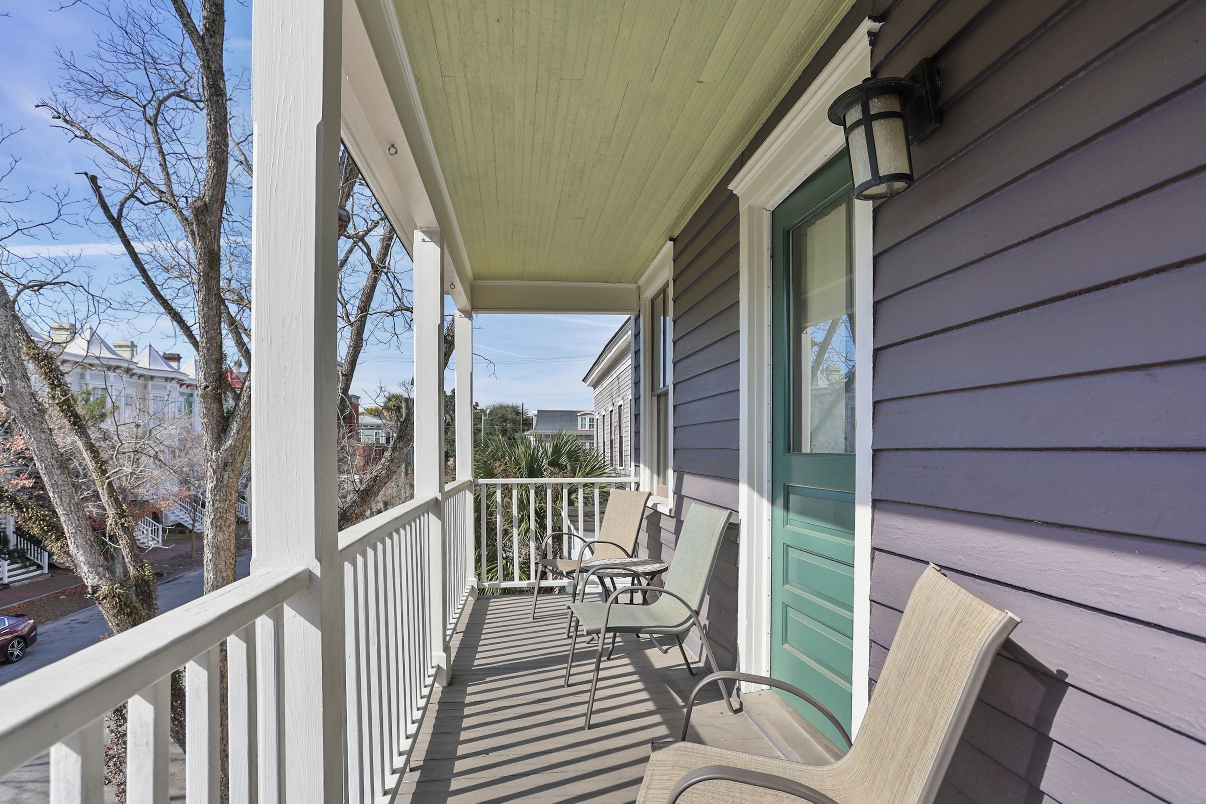 A covered porch with a railing, two chairs, and a door with a green trim.