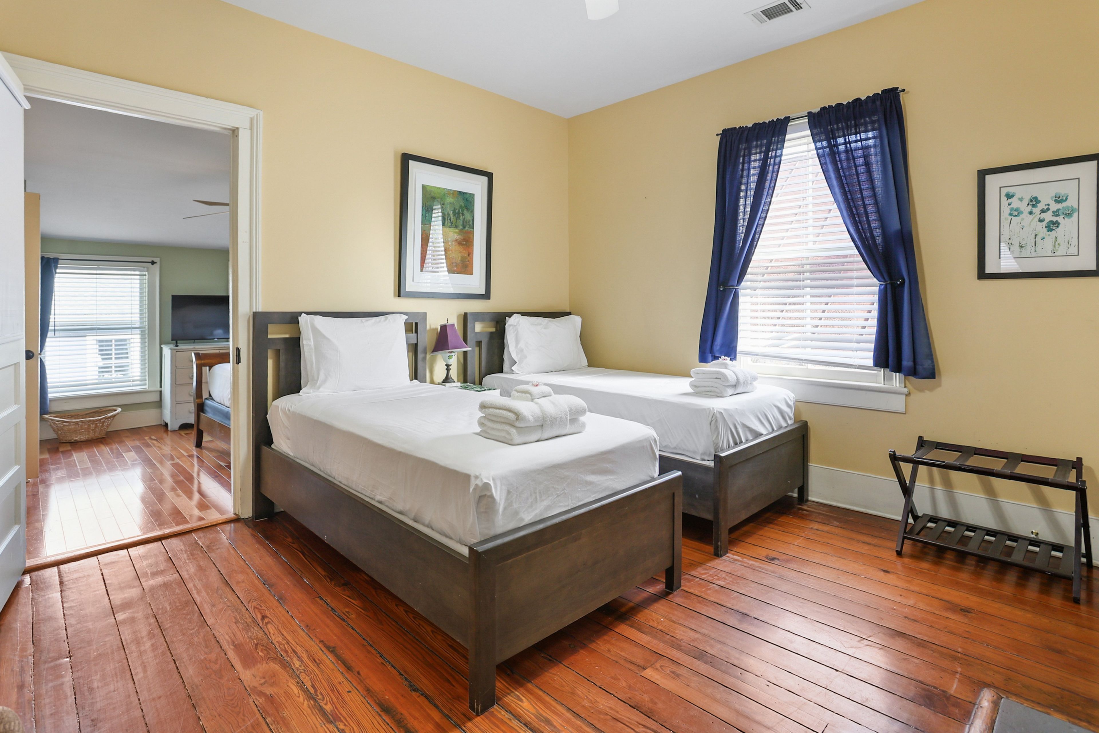 Une chambre d’hôtel avec deux lits, un plancher en bois, une petite table et une fenêtre avec des rideaux.