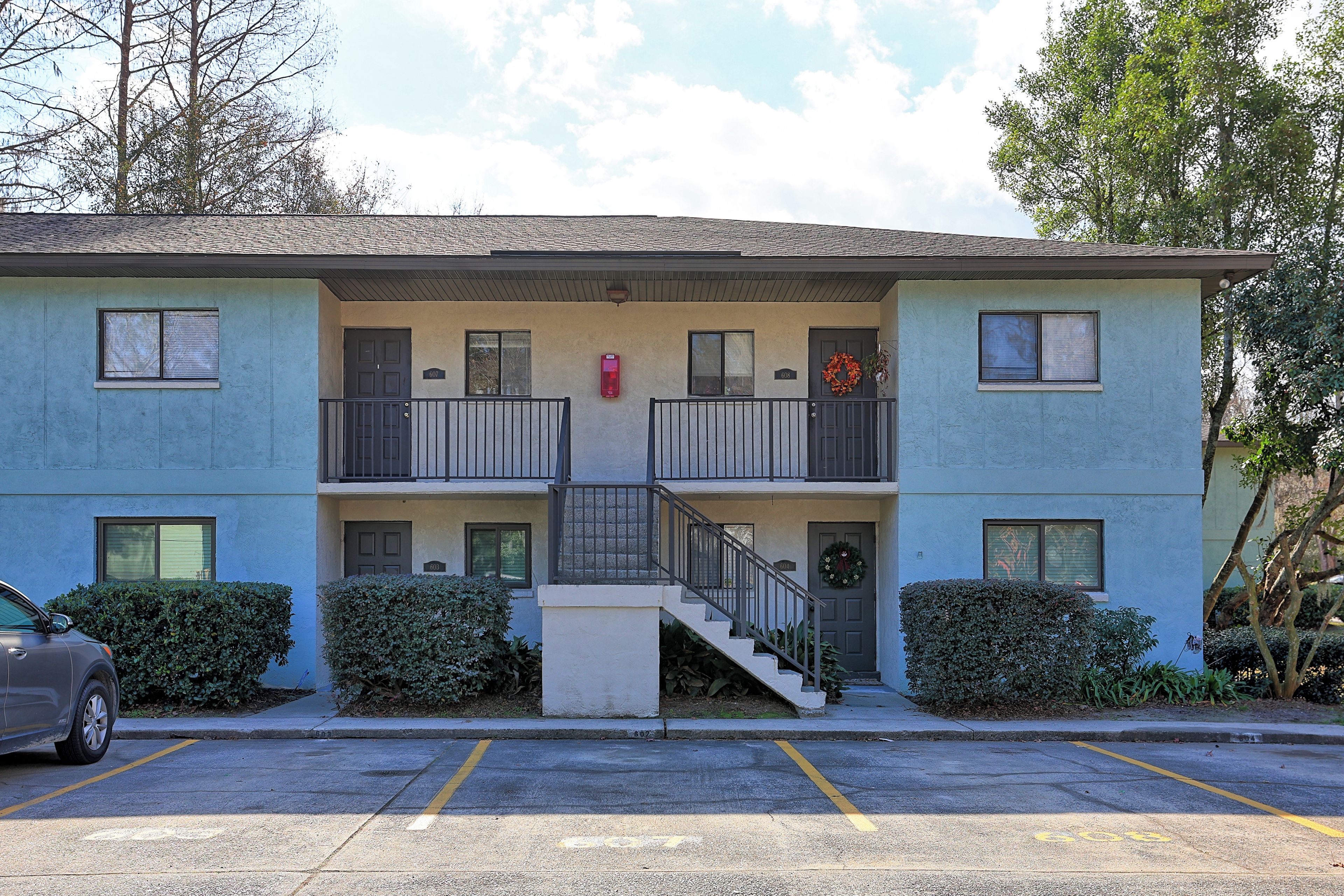 A two-story building with a central staircase, a small balcony on the second floor, and a parking lot in front.