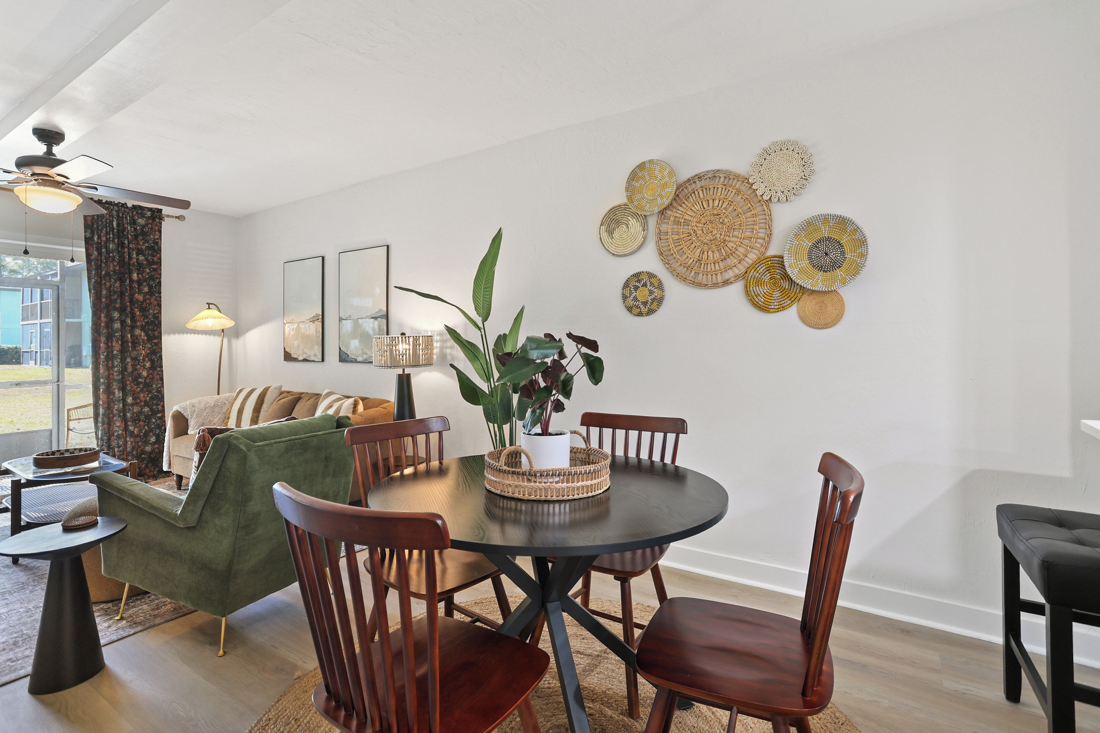 A dining area with a round table, wooden chairs, a green sofa, and a ceiling fan.