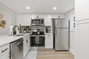 A modern kitchen with white cabinets, stainless steel appliances, and a tiled backsplash.
