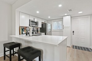 A modern kitchen with white cabinetry, a central island, and two black bar stools. - Savannah, 2bed/2bath, Pet Friendly (Savannah)